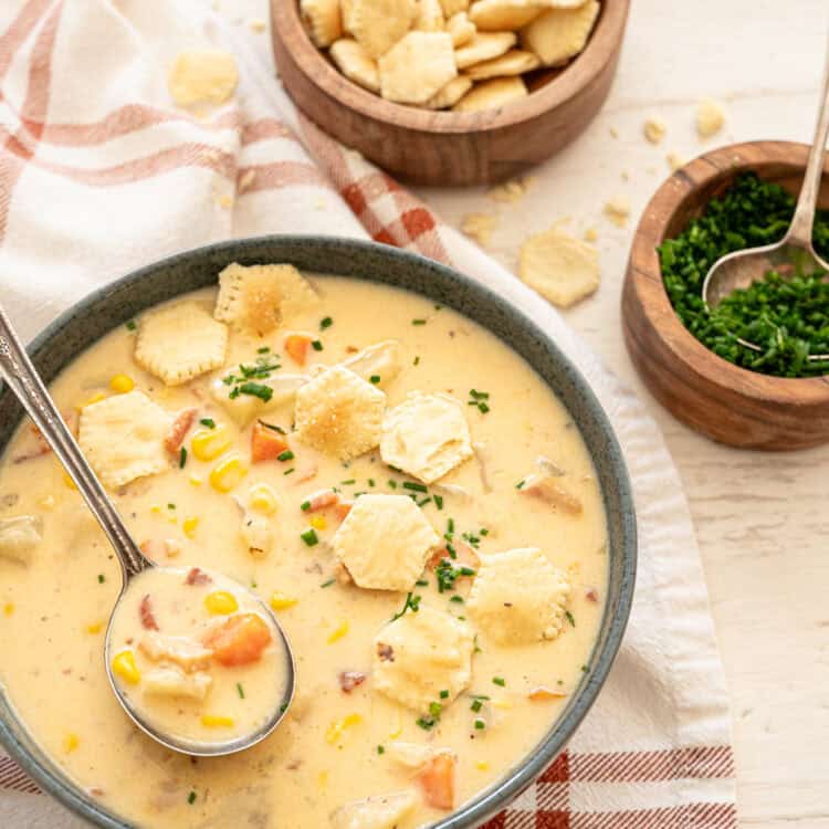 Potato corn chowder in a gray bowl with oyster crackers and chopped chives on top.