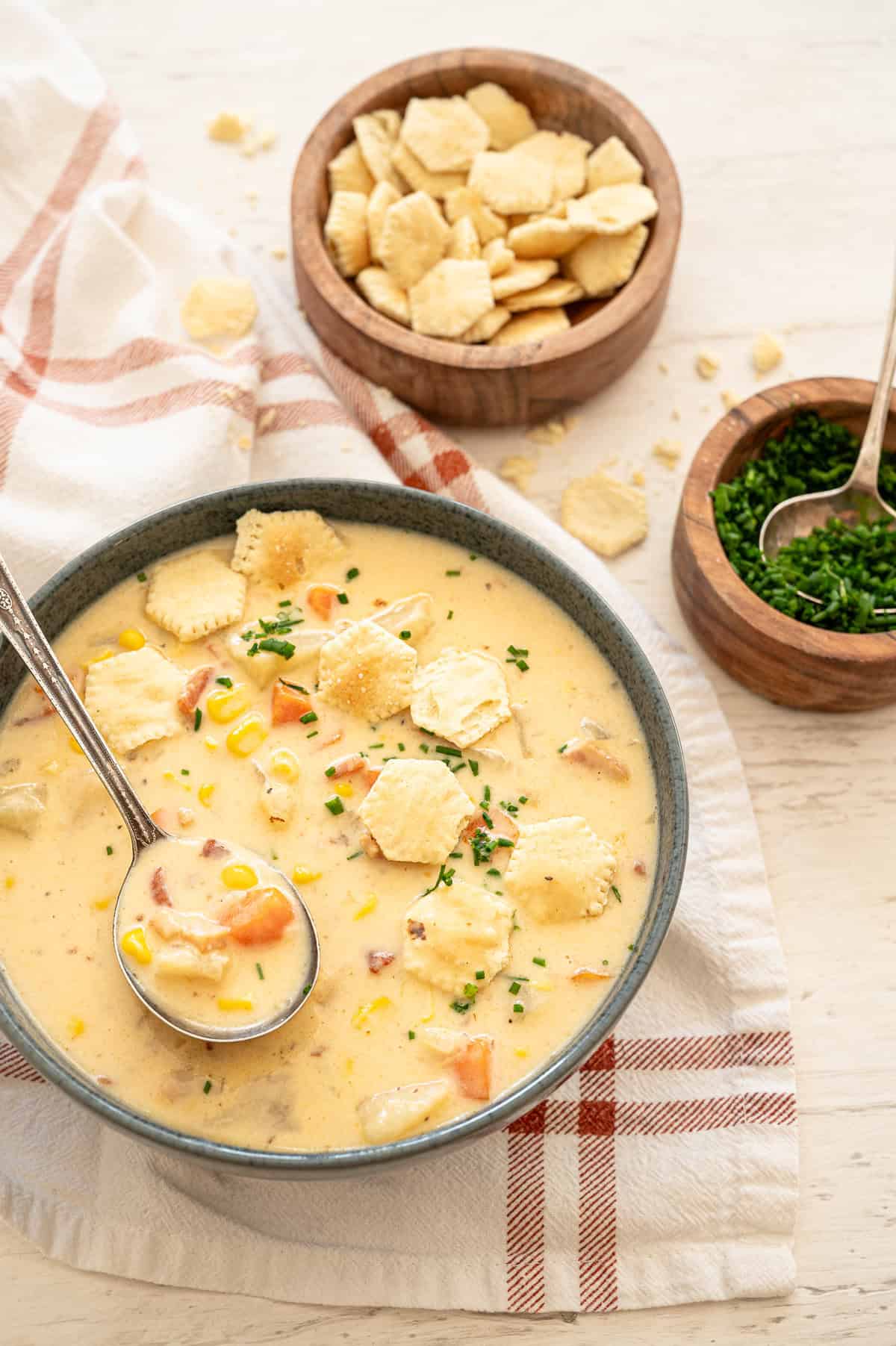 Potato corn chowder in a gray bowl with oyster crackers and chopped chives on top.