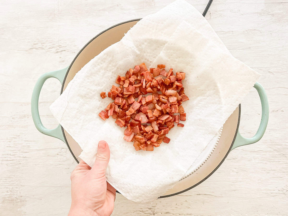 A hand holding a paper towel over a pot with cooked chopped bacon on top.