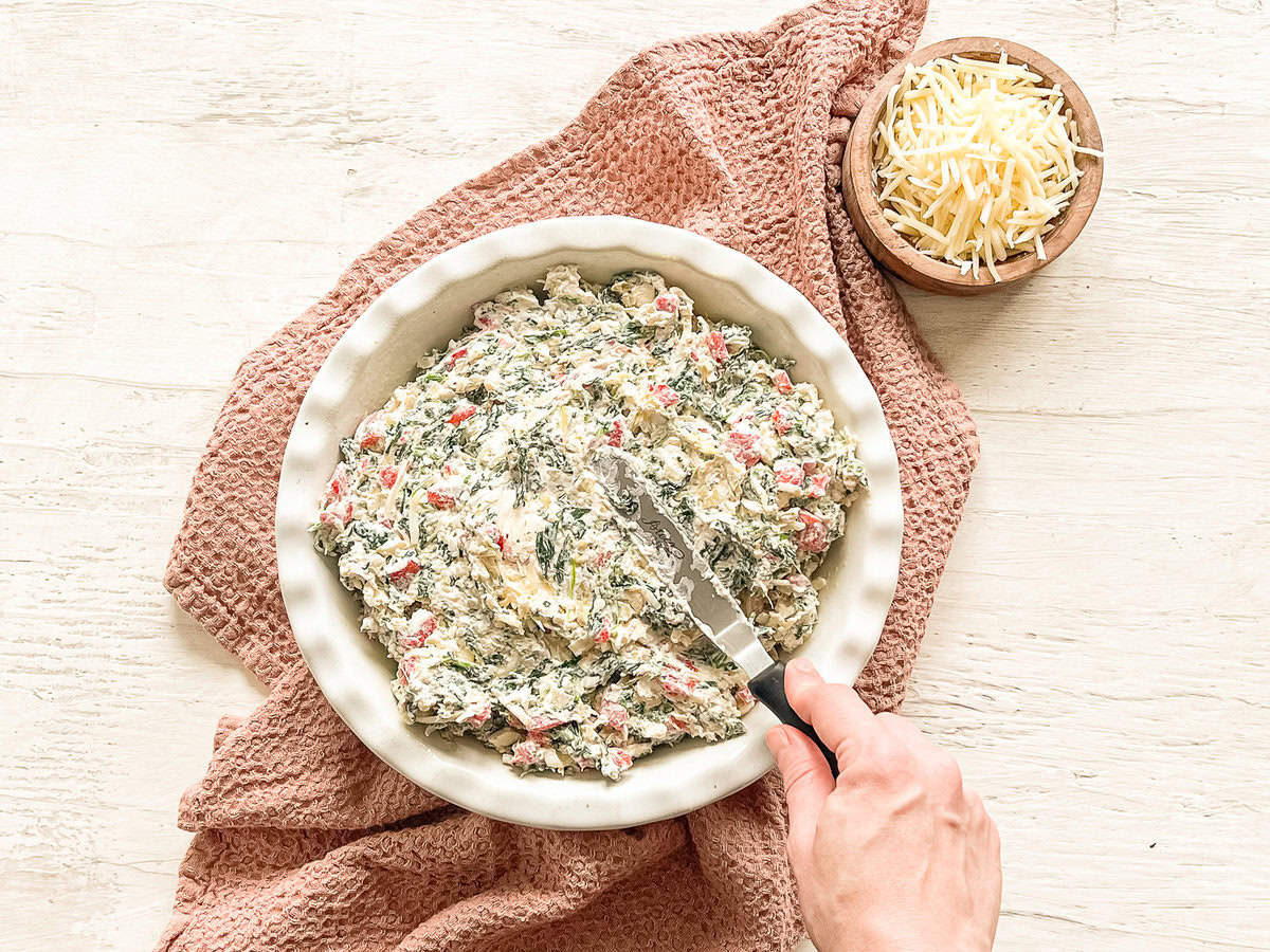 Spinach and artichoke dip being spread in a shallow crock.