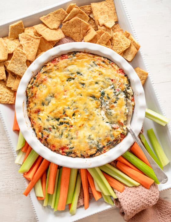 A platter of celery, carrots, and crackers with baked Spinach and Artichoke Dip in the middle.