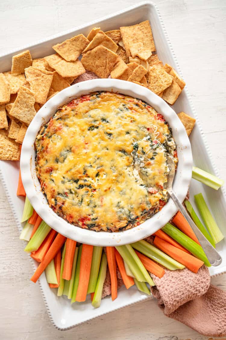 A platter of celery, carrots, and crackers with baked Spinach and Artichoke Dip in the middle.