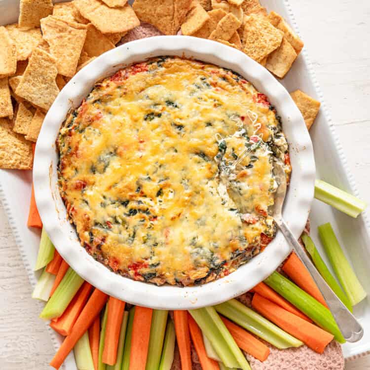 A platter of celery, carrots, and crackers with baked Spinach and Artichoke Dip in the middle.