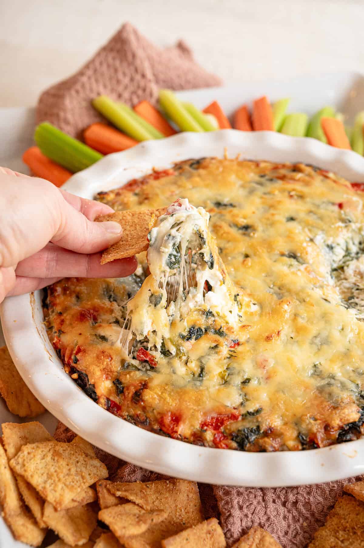 A cracker lifting some spinach and artichoke dip out of the crock it was made in.