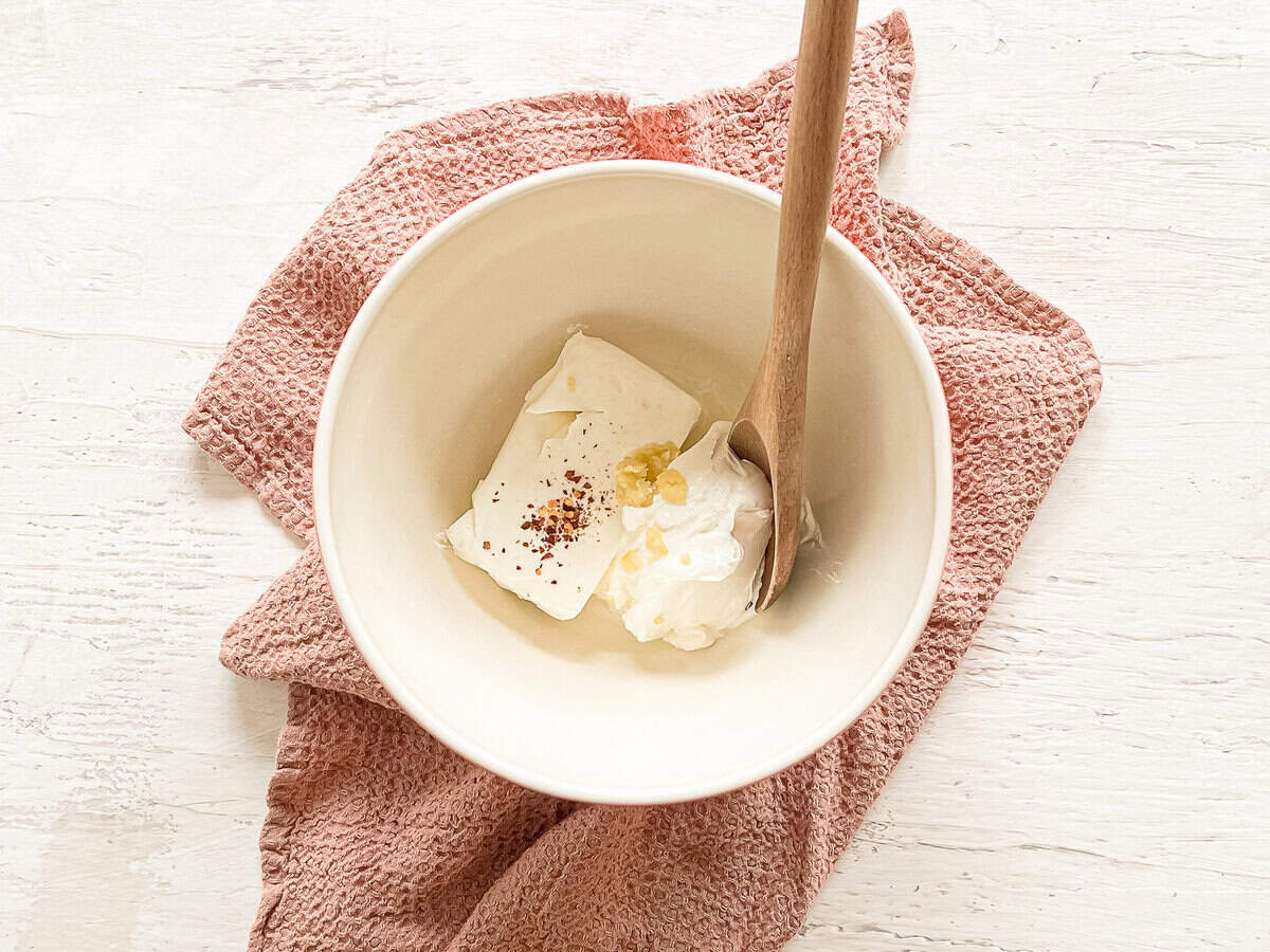 A bowl with cream cheese, red pepper flakes, minced garlic and lemon juice waiting to be mixed.