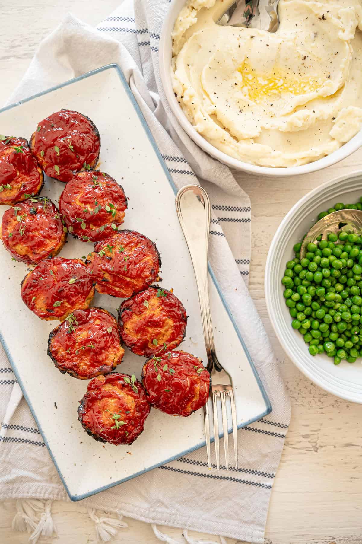 Turkey meatloaf muffins on a platter with a bowl of mashed potatoes and another one with peas next to it.