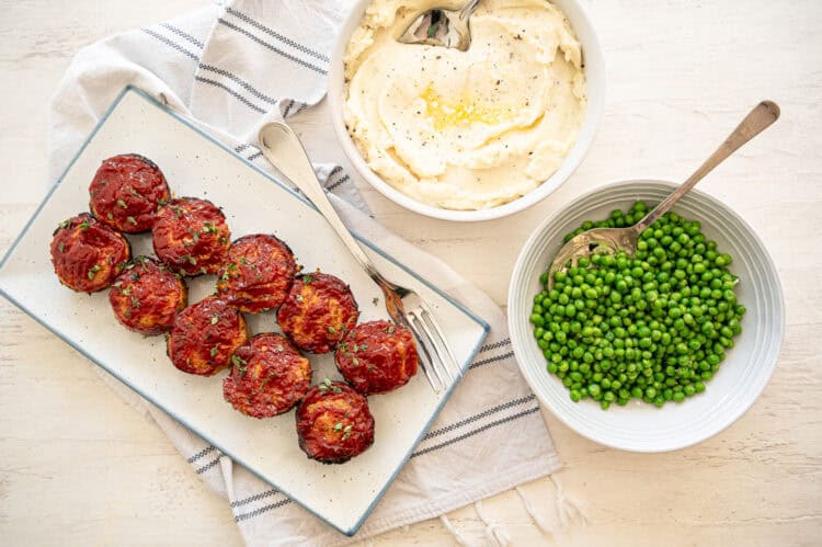 Turkey meatloaf muffins on a platter with bowls of peas and mashed potatoes next to it.