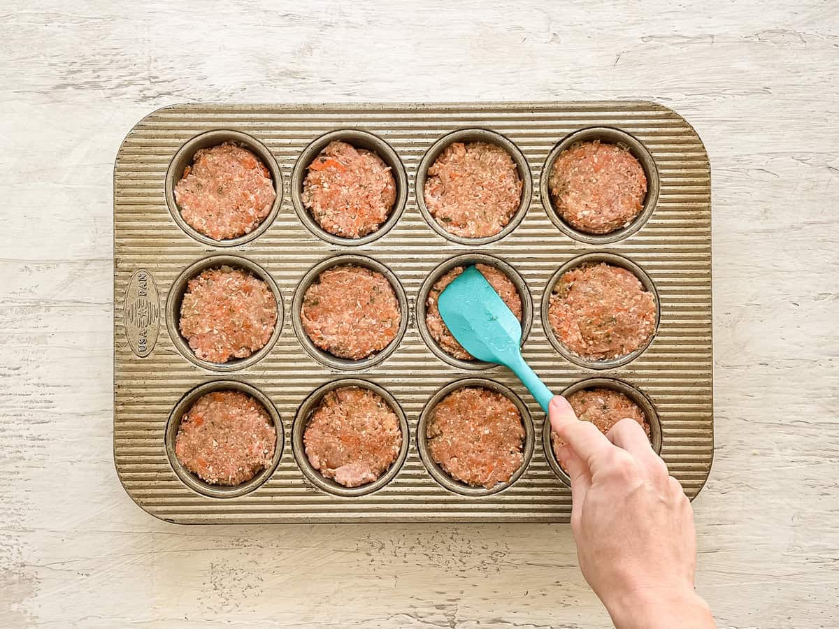 Turkey meatloaf muffin mixture being pushed into a muffin tin.