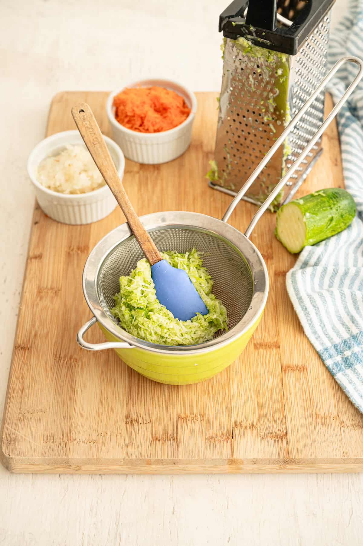 Shredded zucchini being pushed in a colander to remove excess liquid.