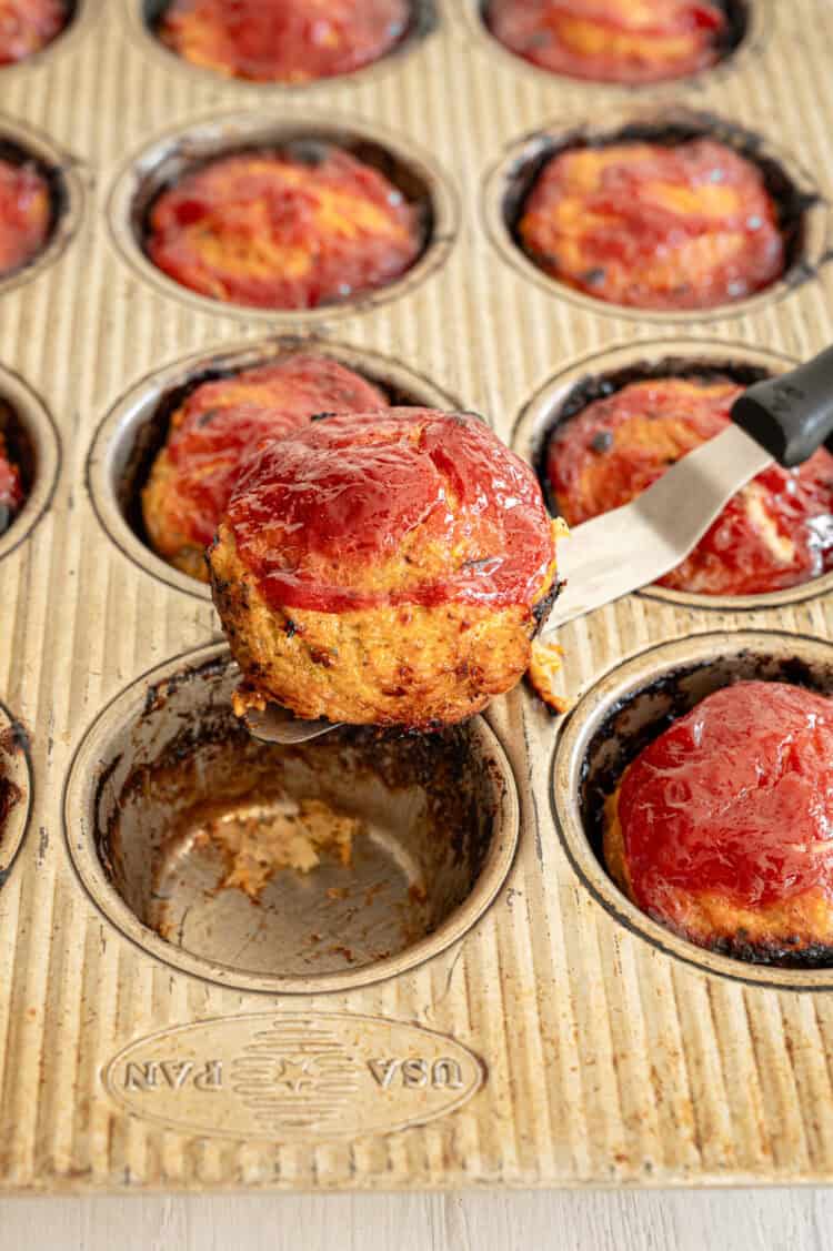 A turkey meatloaf muffin being lifted from the muffin tin ready to serve.