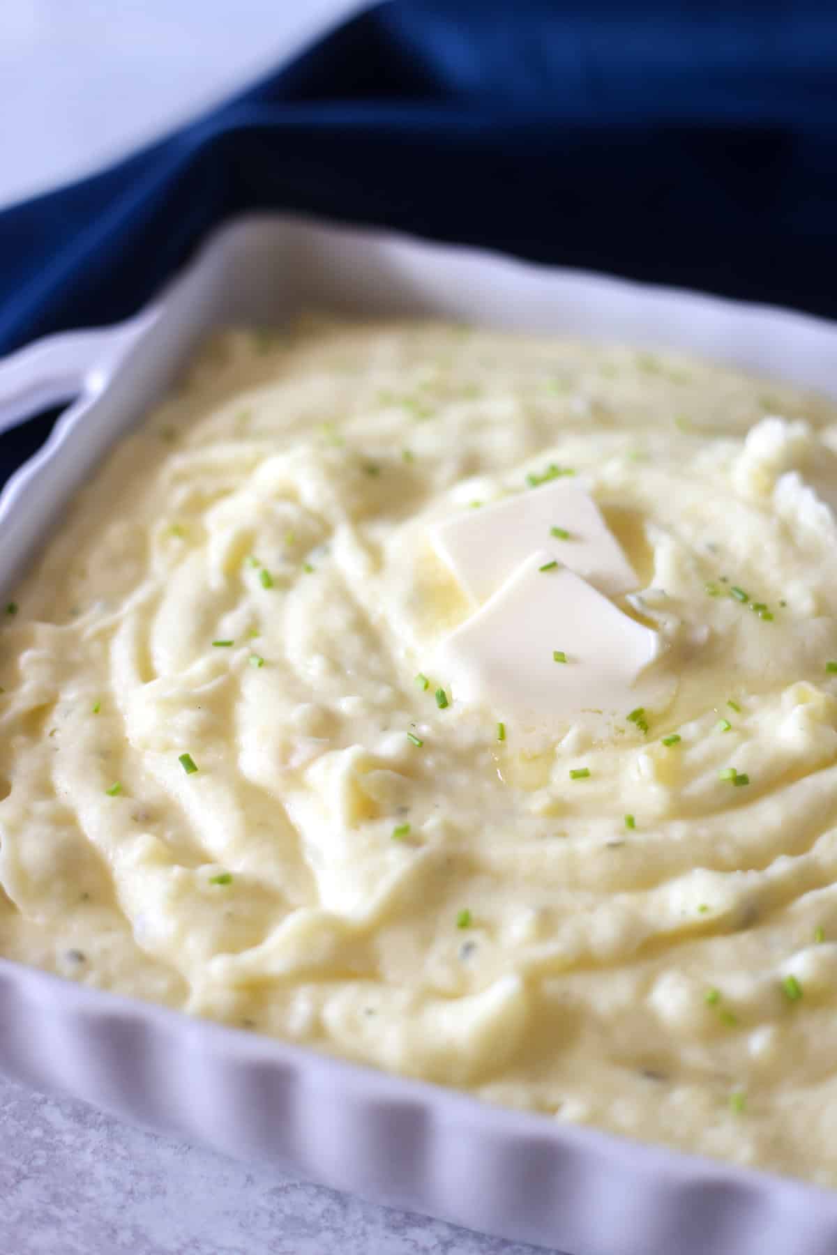 Creamy gourmet mashed potatoes with 2 pats of butter and chopped chives on top.