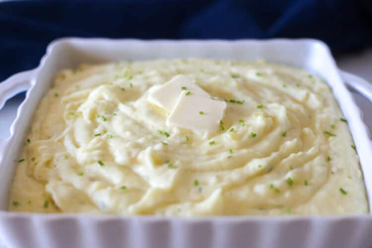 Two pats of butter and fresh chopped chives on top of gourmet Boursin mashed potatoes ready to serve.