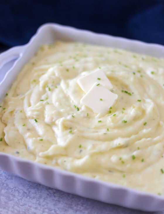 Creamy gourmet mashed potatoes with butter pats and chopped chives on top.