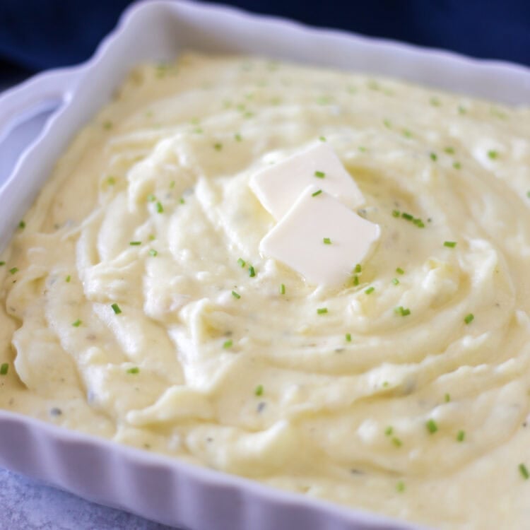 Creamy gourmet mashed potatoes with butter pats and chopped chives on top.