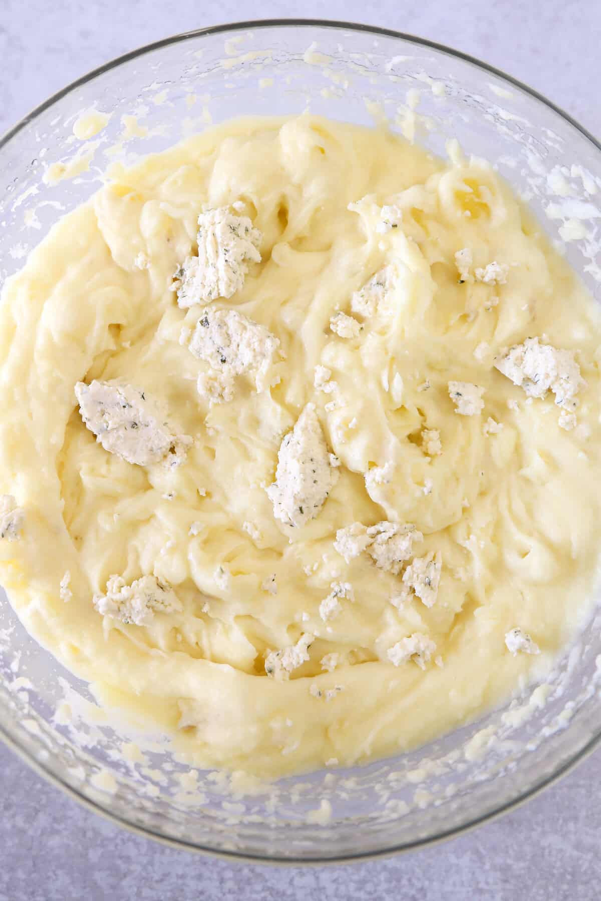 Mashed potatoes in a bowl with chunks of Boursin cheese waiting to be mixed in,