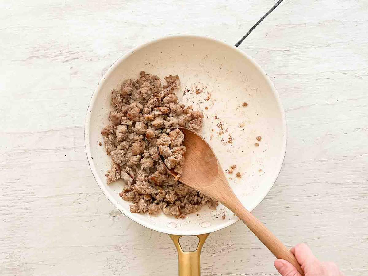 A wooden spoon stirring ground turkey sausage in a skillet.