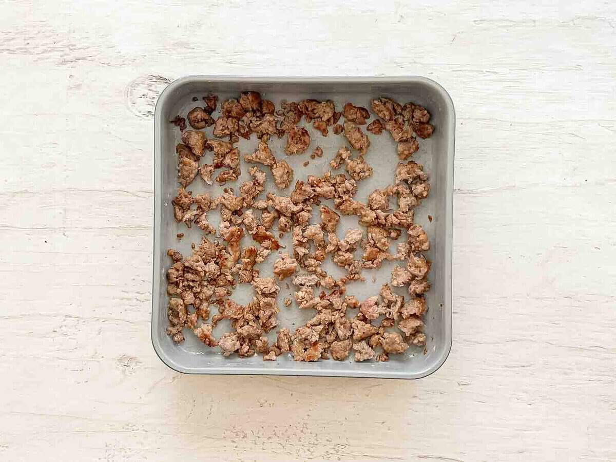 Cooked ground turkey sausage on the bottom of a 9x9 baking dish.