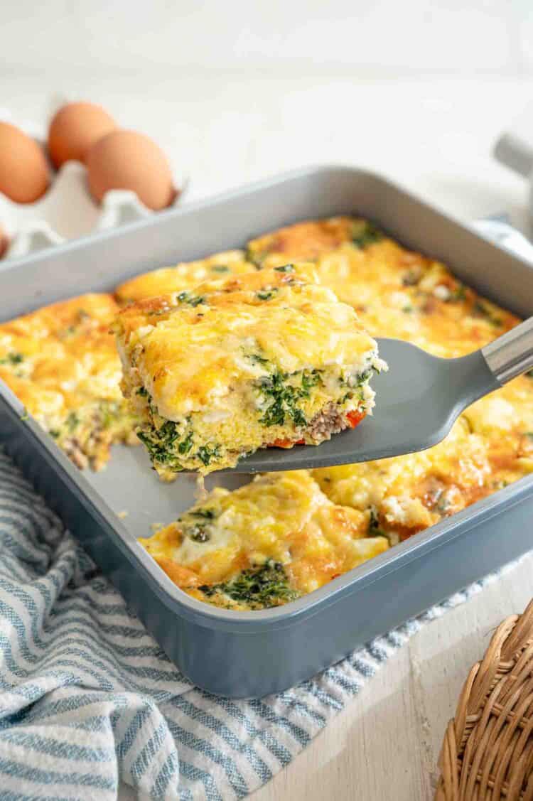 A spatula lifting a slice of Mediterranean high protein low carb breakfast casserole from the baking dish.