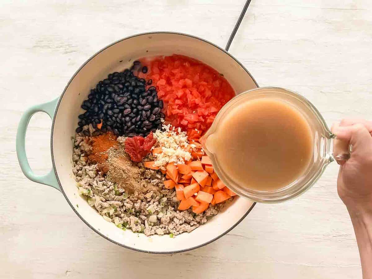 Chicken broth being poured into a pot with the rest of the ingredients for turkey chili with sweet potatoes.