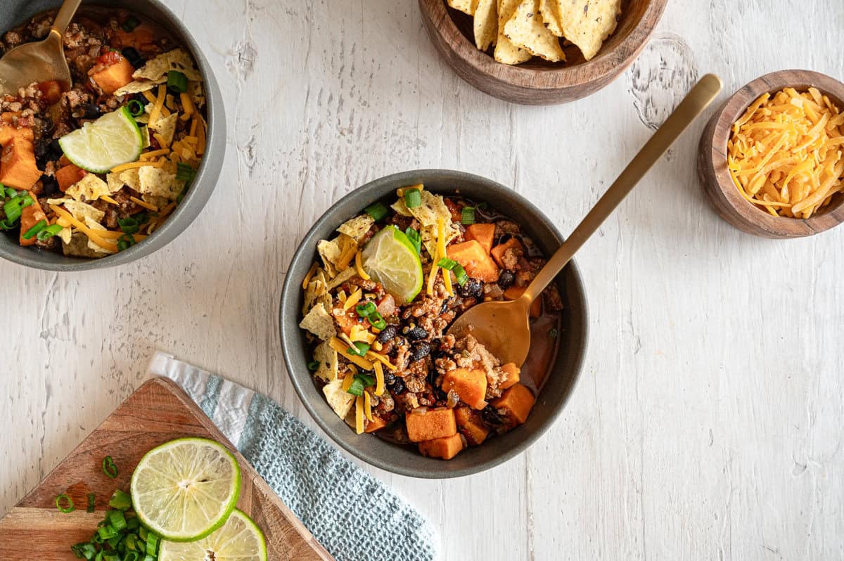 Bowls of easy turkey chili with chopped chives, shredded cheese, and crushed tortilla chips on top.