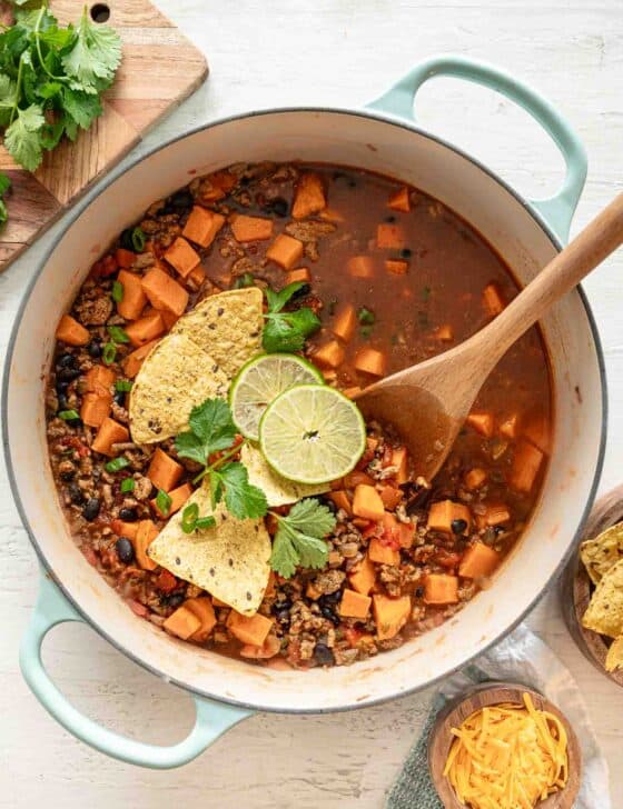 Turkey chili in a pot with tortilla chips, lime slices and fresh cilantro on top.