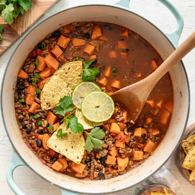 Turkey chili in a pot with tortilla chips, lime slices and fresh cilantro on top.