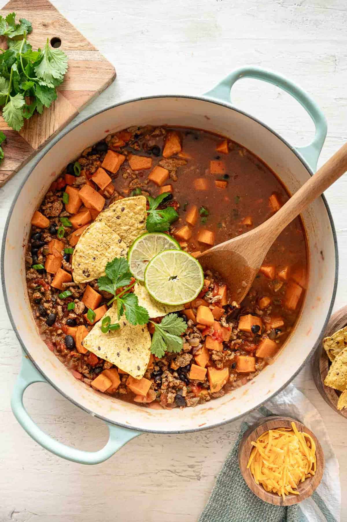 Easy Turkey chili with sweet potatoes in a pot with tortilla chips, lime slices and fresh cilantro on top.