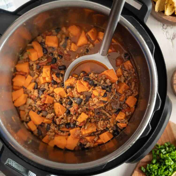 A spoon lifting a serving of turkey and sweet potato chili out of an Instant Pot.