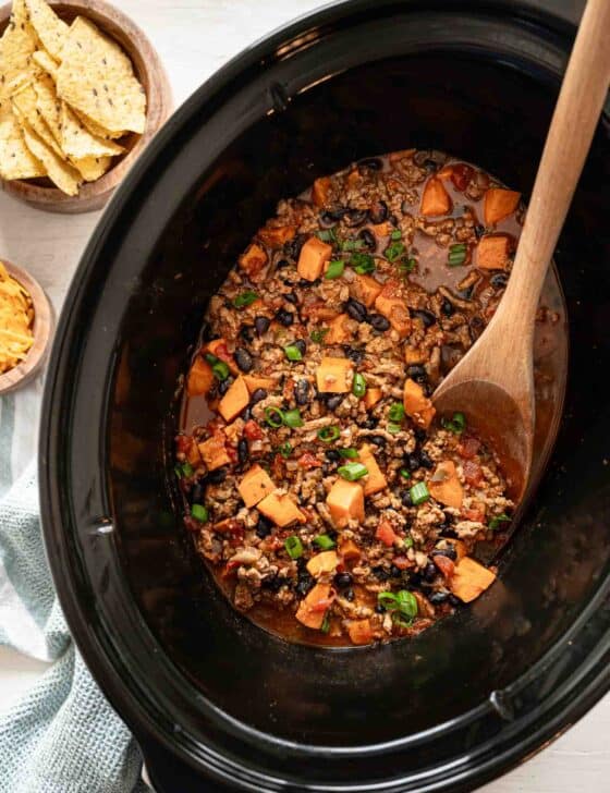 A wooden spoon lifting a serving of turkey chili out of a slow cooker.