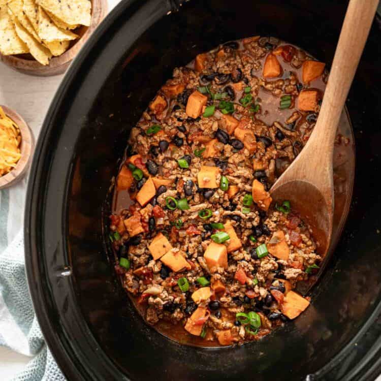 A wooden spoon lifting a serving of turkey chili out of a slow cooker.