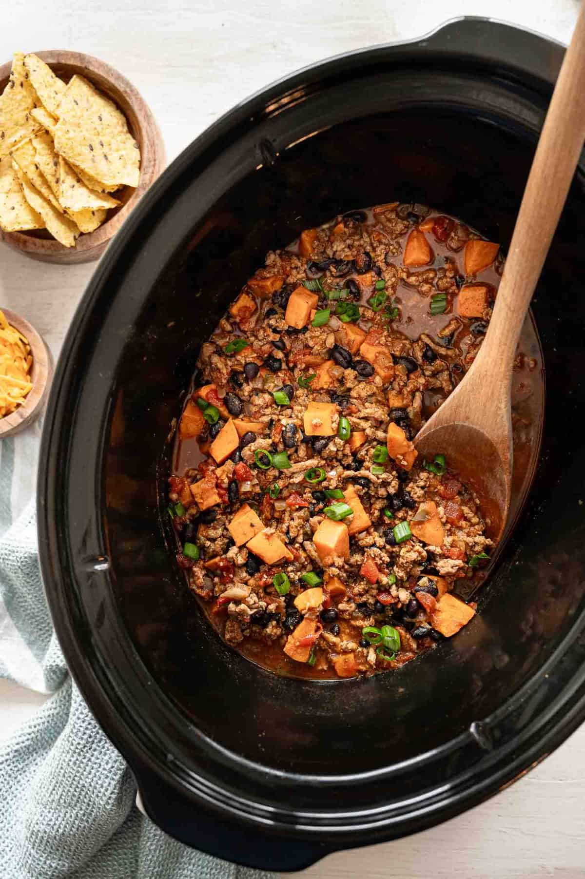 A wooden spoon lifting a serving of turkey chili out of a slow cooker.