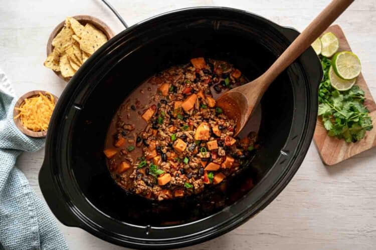 Turkey and sweet potato chili in a slow cooker with chopped chives on top.