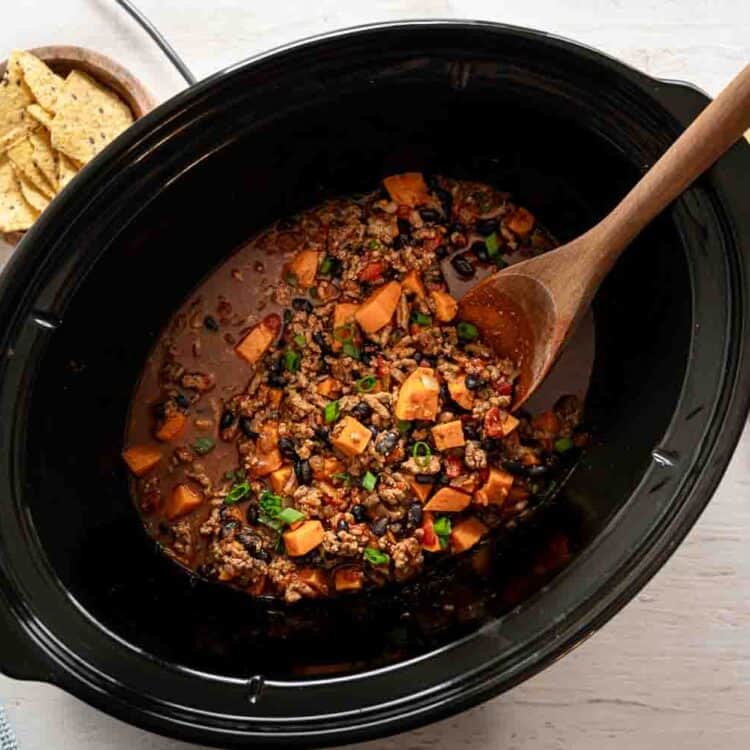 Turkey and sweet potato chili in a slow cooker with chopped chives on top.