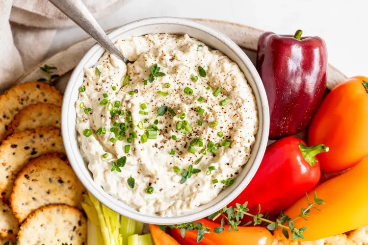 Creamy caramelized onion dip in a bowl with fresh veggies.