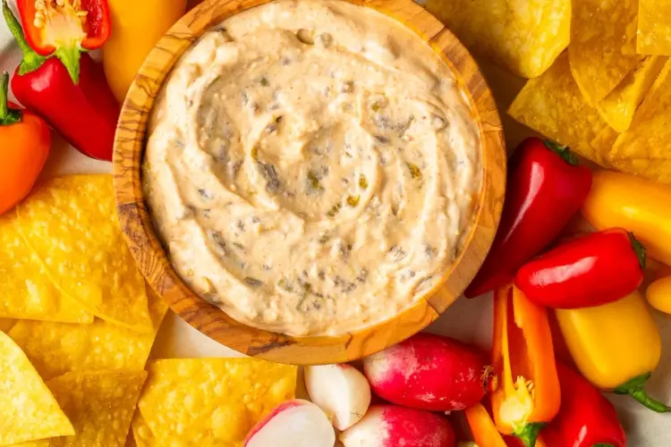 Cottage queso dip in a wooden bowl with fresh veggies and tortilla chips around it.