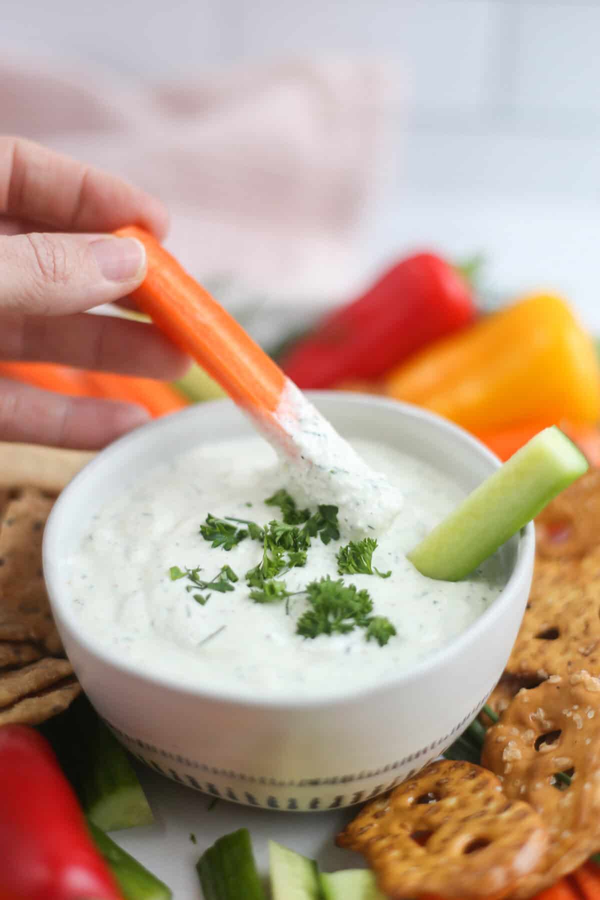 A hand dipping a carrot stick into cottage cheese ranch dip.