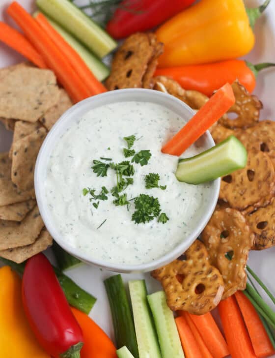 A carrot stick and a cucumber spear sticking out of a bowl of cottage cheese ranch dip.