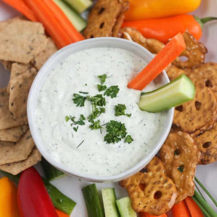 A carrot stick and a cucumber spear sticking out of a bowl of cottage cheese ranch dip.