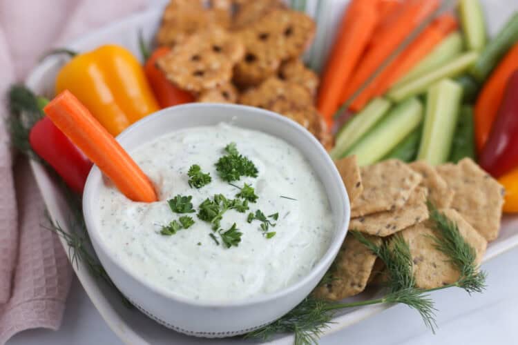 Cottage cheese ranch dip in a bowl on a platter of crackers and veggie sticks.