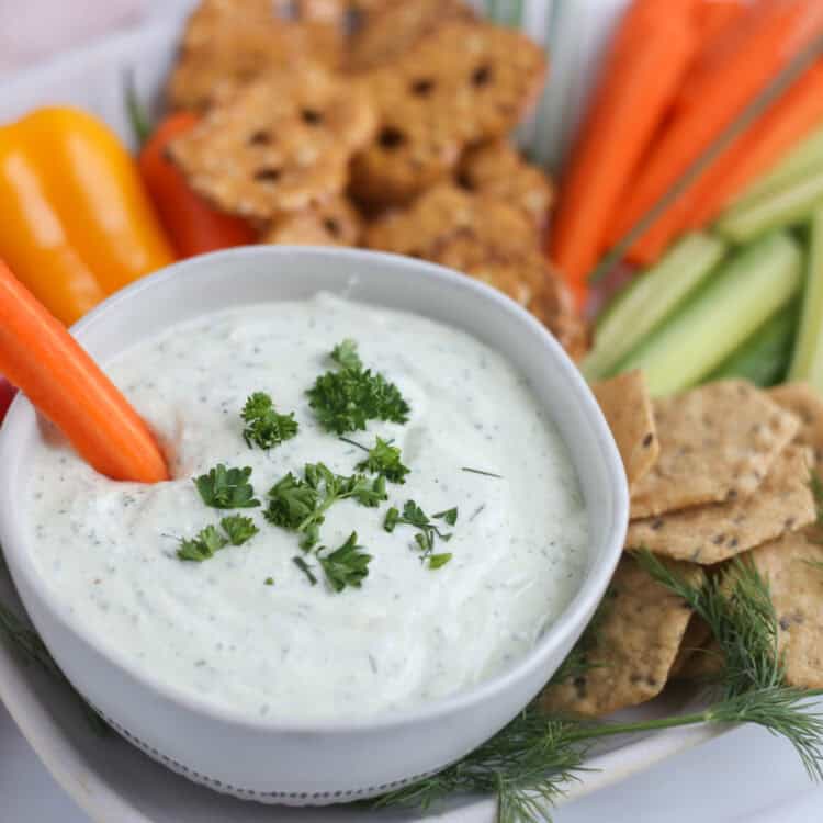 Cottage cheese ranch dip in a bowl on a platter of crackers and veggie sticks.