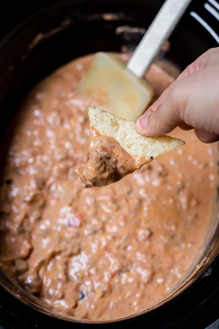 A hand dipping a chip into taco dip in the crockpot.