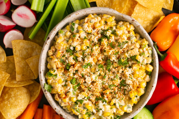 Corn dip in a bowl with fresh veggies and crackers around it.