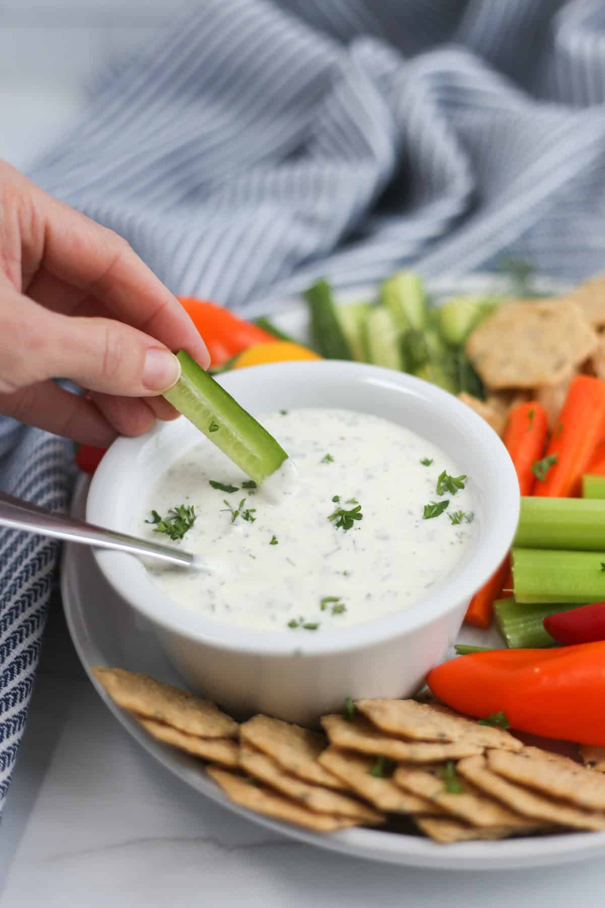 A hand dipping a cucumber spear into homemade ranch dip.