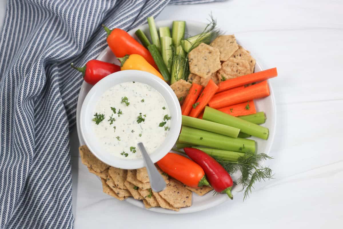 A plate of fresh veggies and crackers with a bowl of homemade ranch dip.