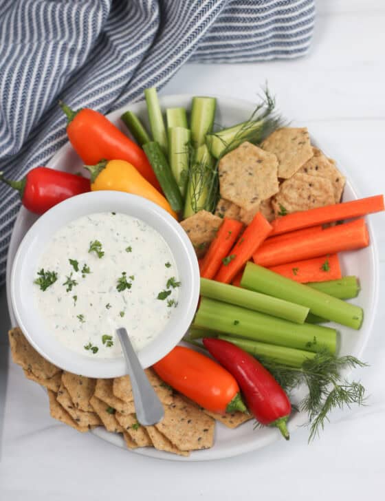 Veggie sticks and crackers on a plate with a bowl of homemade ranch dip.