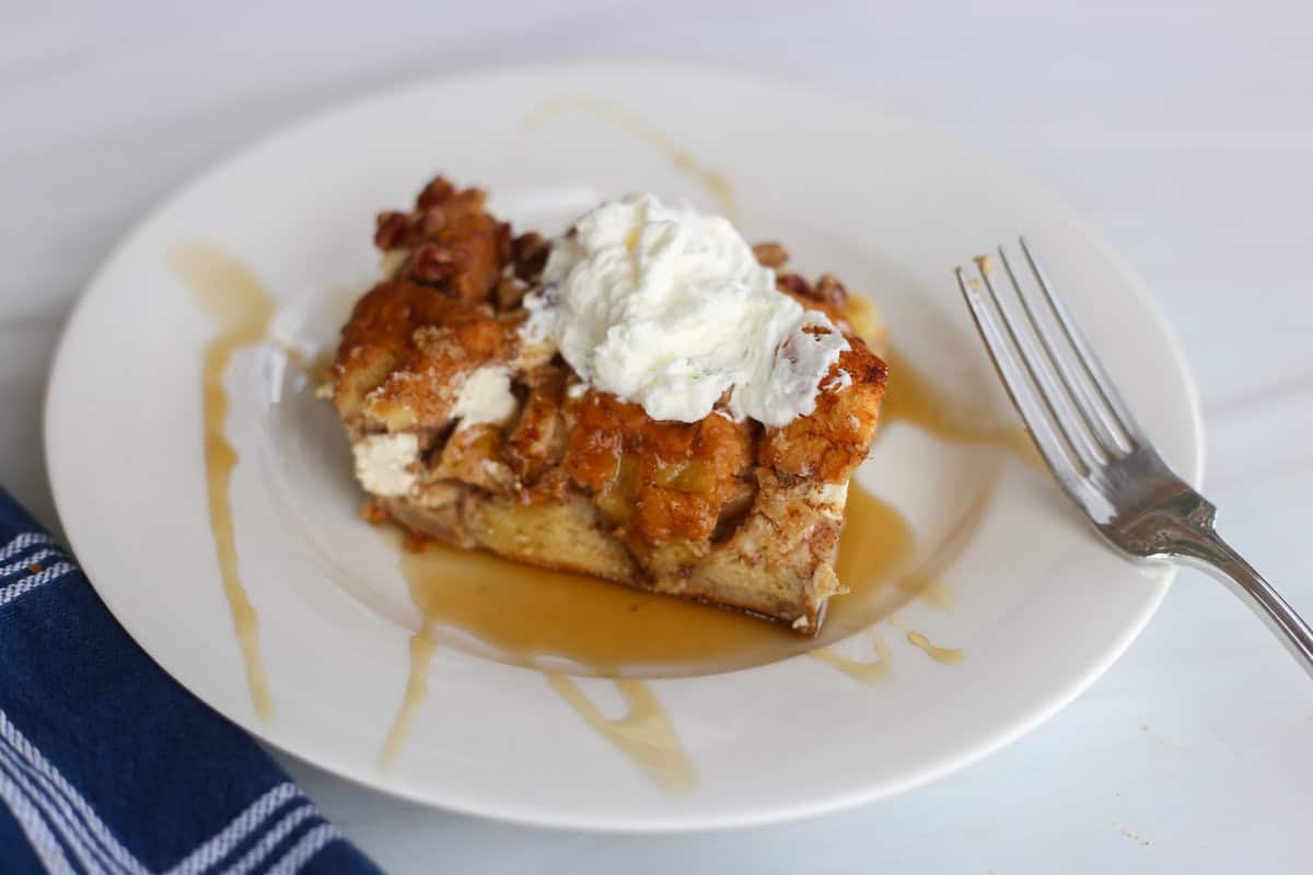 A white plate with a piece of apple cinnamon french toast casserole and a fork on it.