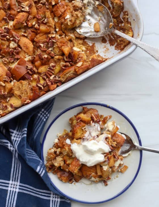 A baking dish of apple cinnamon french toast casserole with a serving of it on a plate next to it.