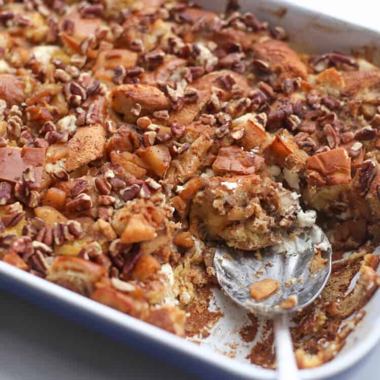 A spoon taking a serving out of a baking dish of apple cinnamon french toast casserole.