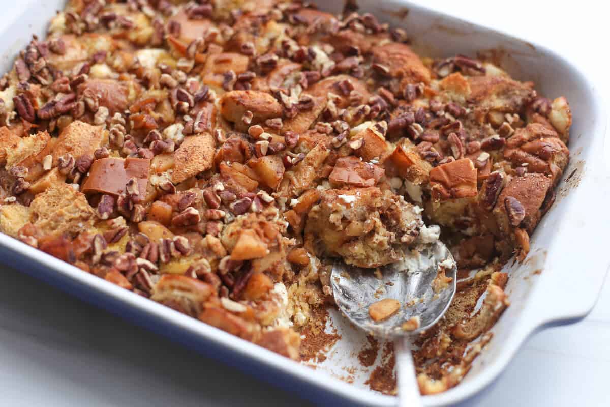 A spoon taking a serving out of a baking dish of apple cinnamon french toast casserole.