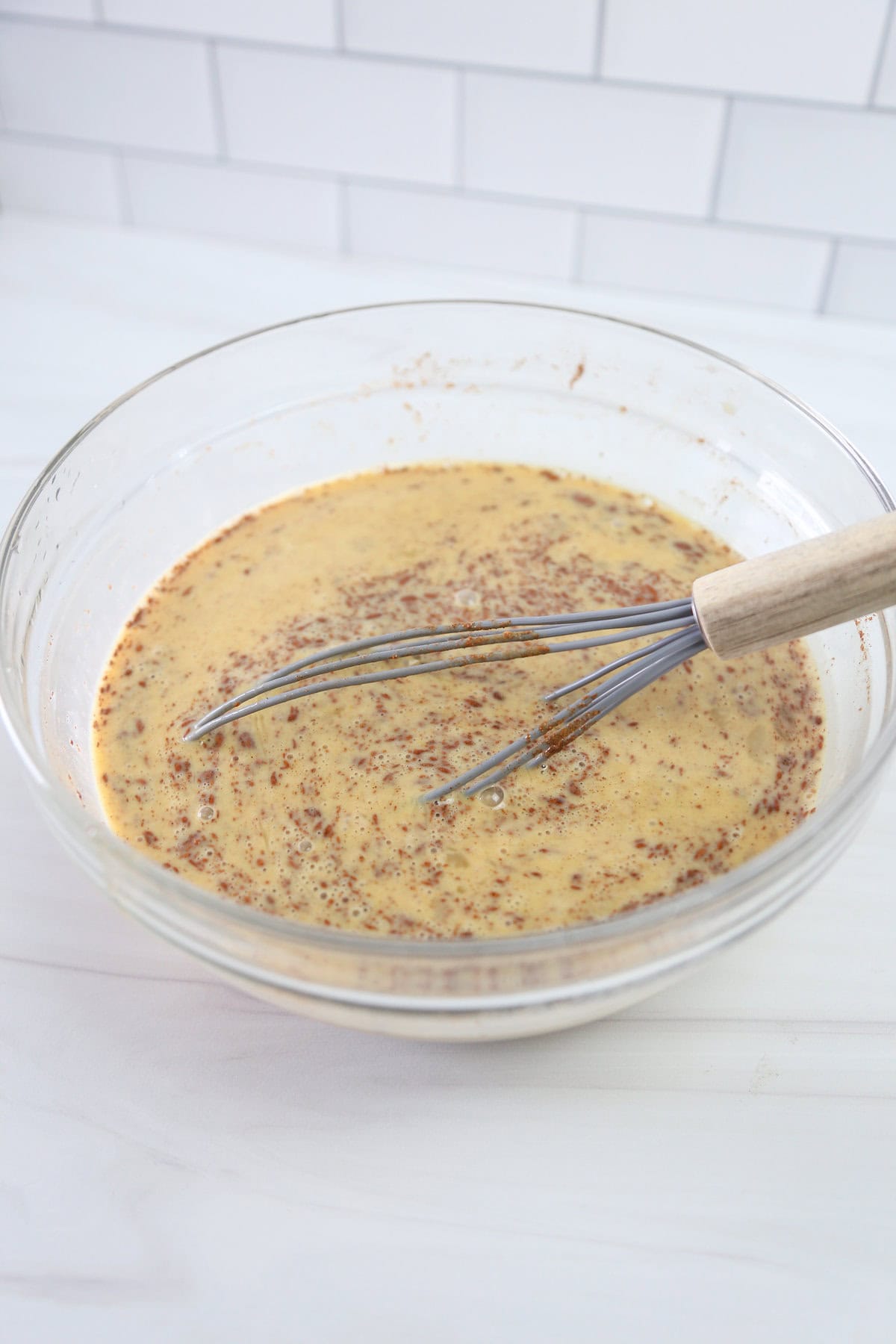 Beaten eggs and cinnamon in a mixing bowl with a whisk.